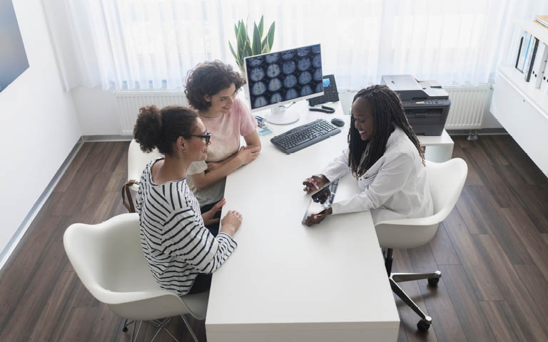 PHOTO: Female doctor telling mother and daughter medical results at doctors office using digital tablet 