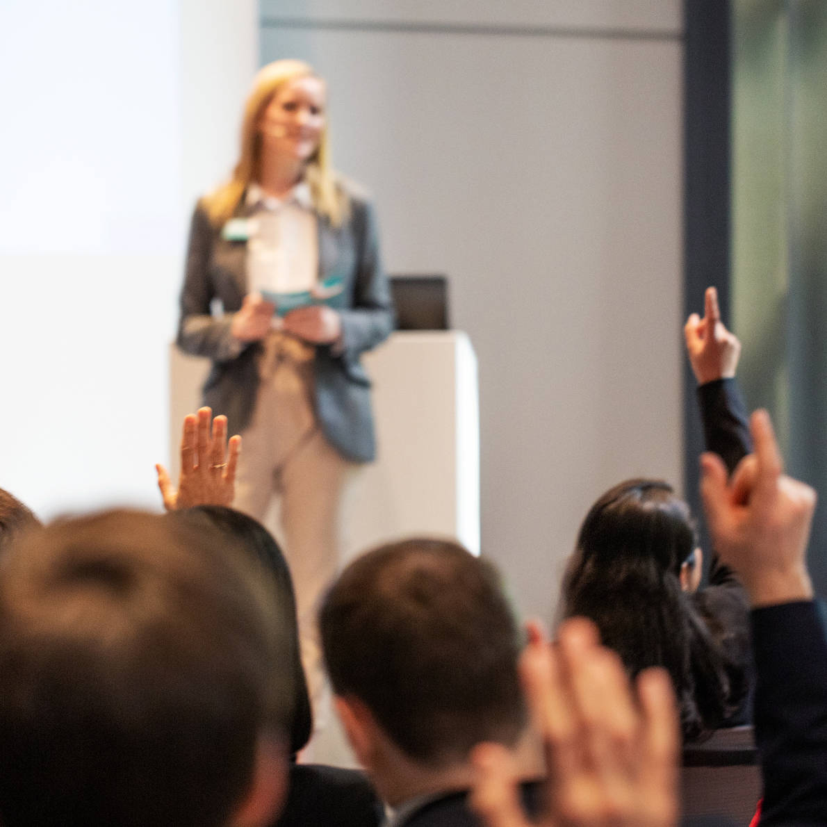 Woman presenting on stage in front of crowd raising their hands to ask questions
