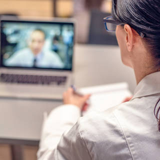 woman in white coat taking notes while watching webinar