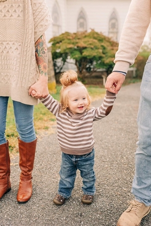 Photo of toddler holding hand of each parent